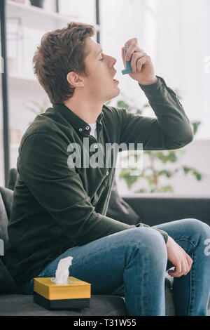 handsome man using inhaler while sitting on sofa Stock Photo