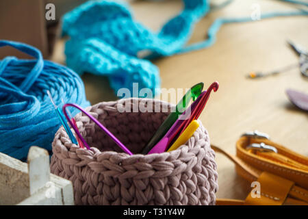 Two-tone knitted basket on a light wooden surface against the background of knitting and details for making handmade knitted bags. Selective soft focu Stock Photo