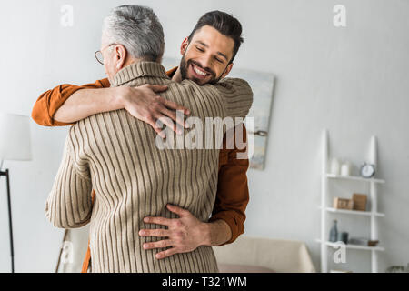 happy bearded man smiling while hugging elder father at home Stock Photo