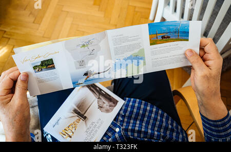 Paris, France - Mar 30, 2019: View from above of senior man holding reading new advertising leaflet from CroisiEurope an international river cruise company to South Africa Stock Photo