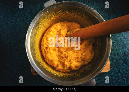 Polenta or mamaliga and beech wood stirrer in cast iron pot (cooper pot).  Traditional dish prepared by boiling water, salt, cornmeal. Substitute for  Stock Photo