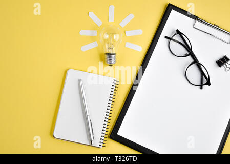 Financial planning table top with pen, notepad, eyeglasses and light bulb on yellow background. Concept brainstorming and new idea Stock Photo