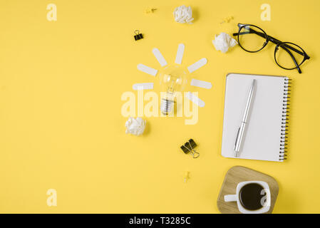 Office workspace with blank clip board, office supplies, pen, notepad, eyeglasses, coffee cup and light bulb on yellow background. Concept brainstormi Stock Photo