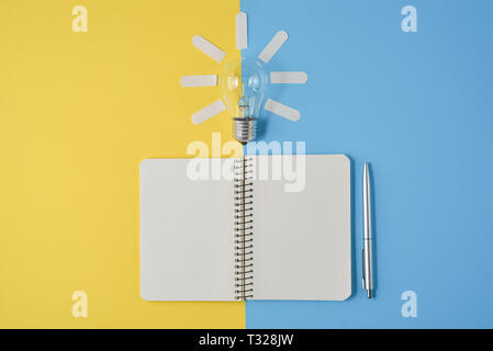 Financial planning table top with pen, notepad, light bulb on yellow and blue background. Concept brainstorming Stock Photo