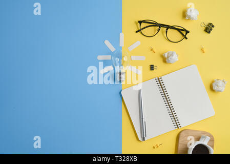 Financial planning table top with blank clip board, office supplies, pen, notepad, eyeglasses, coffee cup, light bulb on yellow and blue background. C Stock Photo