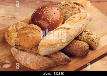 side view of different types of bread piled up on wooden kitchen cutting board Stock Photo