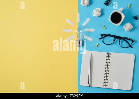 Financial planning table top with blank clip board, office supplies, pen, notepad, eyeglasses, coffee cup, light bulb on yellow and blue background. C Stock Photo
