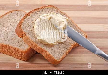 A knife spreading butter on wheat bread Stock Photo