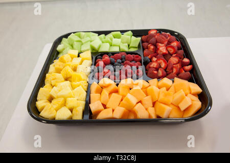 Black plastic tray of cut up fruit for a party on a table Stock Photo