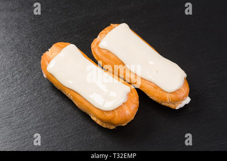 Two eclairs with white icing on black background. Stock Photo
