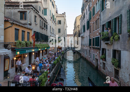 Venice, Italy - June 30, 2018: Panoramic view of Venice canal with historical buildings and gondolas from bridge. People relax and eating in restauran Stock Photo