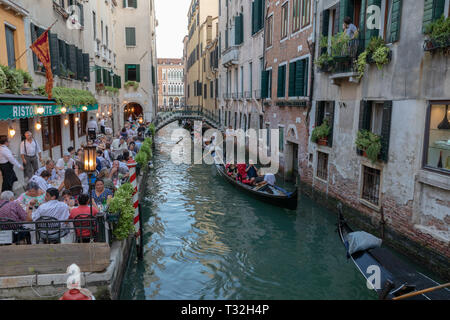 Venice, Italy - June 30, 2018: Panoramic view of Venice canal with historical buildings and gondolas from bridge. People relax and eating in restauran Stock Photo