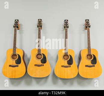 Four acoustic guitars are hung next to each other on a white wall. Stock Photo
