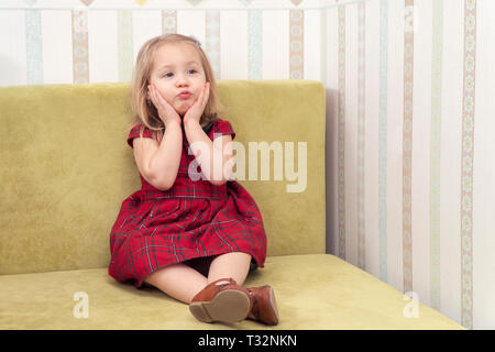 little girl sitting on the couch and holding on to his inflated cheeks Stock Photo
