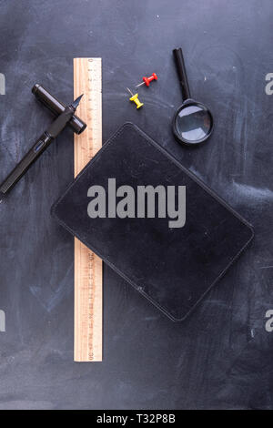 Magnifying glass fountain pen and ruler with a notebook on the blackboard Stock Photo