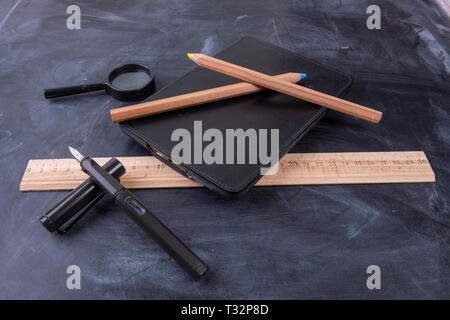 Magnifying glass fountain pen and ruler with a notebook on the blackboard Stock Photo