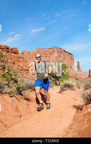 Man jogging with phone in his hand, Park Avenue trail, Arches National Park, Utah, USA. Stock Photo