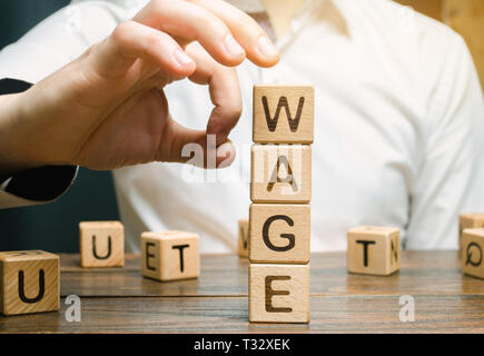 Hand of a businessman removes wooden blocks with the word Wage. Salary reduction concept. Wages cuts. The concept of limited profit. Lack of money and Stock Photo
