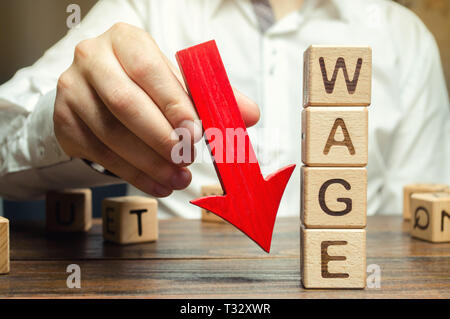 Wooden blocks with the word Wage and red arrow down. Salary reduction. Drop in profits. Financial crisis. Demote. Low profit. Capital outflow. Concept Stock Photo