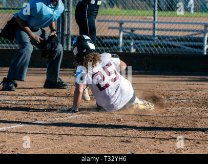 Athletic female softball player sliding safely into home plate under the legs of opponent. Stock Photo