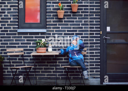 Smiling small boy is sitting on chair on brick wall background Stock Photo