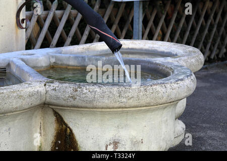 Details of a drinking fountain in Nyon, Switzerland. This fountain is made with light beige concrete and has old black pipe as a tab. Stock Photo