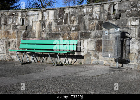 A green bench made of wood and trash can photographed on a sunny spring day in Nyon, Switzerland. In this photo you can also see asphalt walkway. Stock Photo