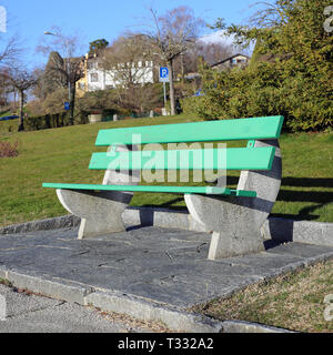 A green bench made of wood and concrete photographed on a sunny spring day in Nyon, Switzerland. In this photo you can also see some grass. Stock Photo