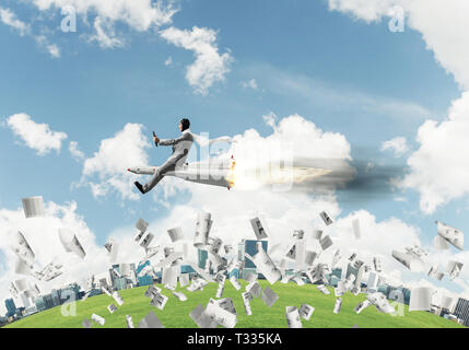 Conceptual image of young businessman in suit flying on rocket among flying papers with cityscape and blue sky on background. Stock Photo