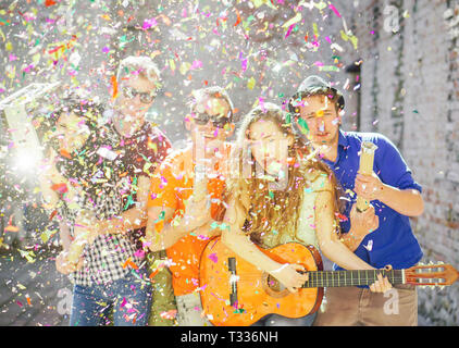 Young friends having a big street party - Group of happy people throwing confetti, playing guitar, singing and dancing on the street Stock Photo