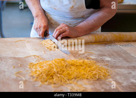 Woman cutting home made tagliolini, traditional italian kind of pasta, made with eggs and flour, on wooden board Stock Photo