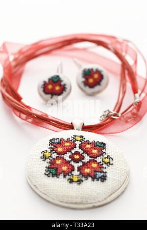 Handmade Cross Stitch Jewelry Set Red Flowers embroidered on white canvas Stock Photo
