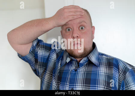 Shocked dazed young man in plaid shirt holding head with a hand. Stock Photo