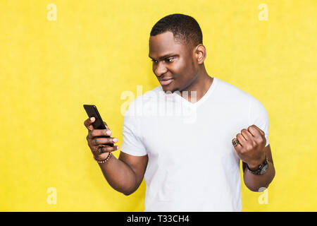 Happy African American man holding smartphone and celebrating his success Stock Photo