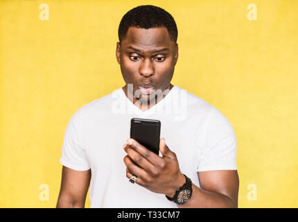 Perplexed and worried handsome African American man holds smartphone, stares with surprised expression Stock Photo