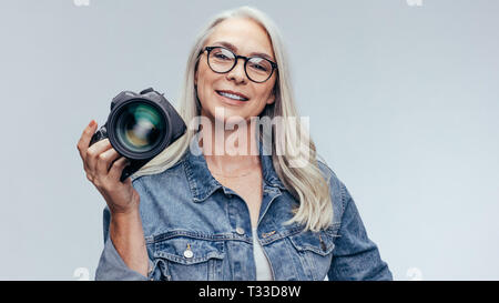 Senior professional photographer holding a DSLR camera. Female photographer with a professional camera on grey background. Stock Photo