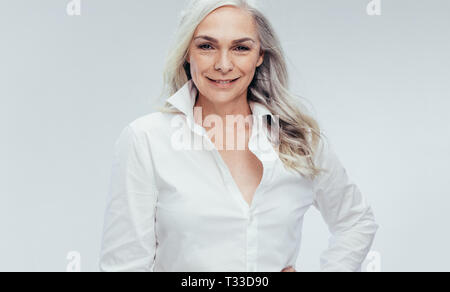 Attractive mature woman posing against white background. Senior woman in white shirt looking at camera. Stock Photo