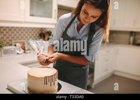 Confectioner decorates cake with chocolate frosting. Cake on kitchen counter with female chef decorating it. Stock Photo