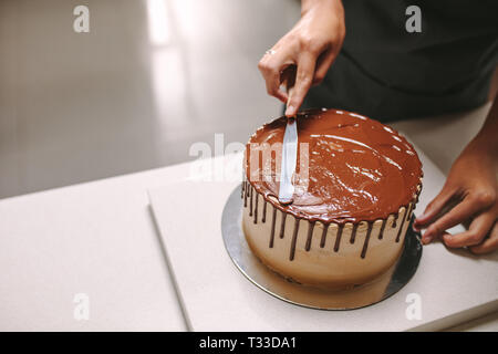 Professional confectioner decorating tasty cake with chocolate frosting on kitchen counter. Pastry chef preparing a chocolate cake. Stock Photo