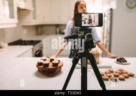 Young female blogger recording video on mobile phone camera in kitchen. Female blogger recording video tutorial session of baking lesson at home kitch Stock Photo