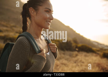 Woman walking on a country path with a backpack. Woman wearing sweater and backpack on hiking in nature. Stock Photo