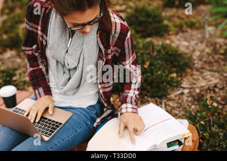Girl student preparing for exams at college campus. Female student studying at university campus, reading book and working on laptop.