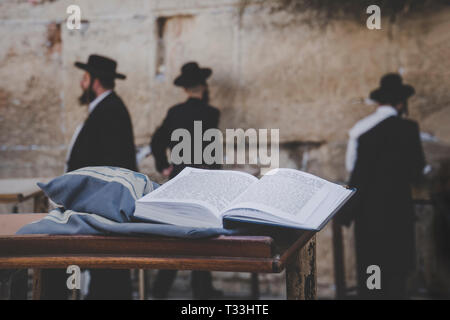 Jewish bible - Torrah open on table on blurred background of praying Jews and wailing western wall. Israel. Jerusalem. Stock Photo