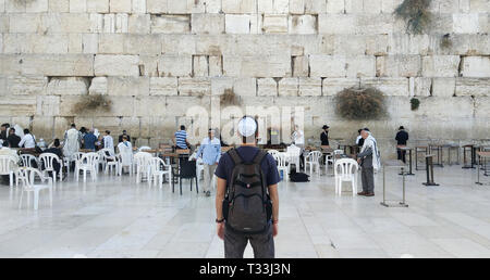 Back of a young tourist in casual clothes and kippah on the head looking at the wailing wall and religious praying near the sacred place of Judaism, J Stock Photo