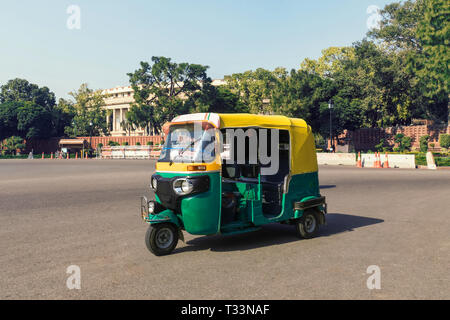 Tuk tuk - traditional indian moto rickshaw taxi on one of the street of New Delhi. yellow green tricycle stands on the square against the background o Stock Photo