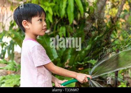 Children are watering plants with rubber hose in the garden. Stock Photo