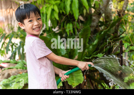 Children happily use the hose to water the trees in the garden. Stock Photo