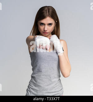 Beautiful boxer girl wearing sportive clothing and gloves practicing in the studio over gray background, athletic body, healthy lifestyle Stock Photo