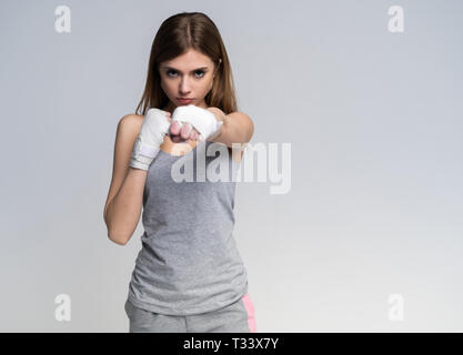 Beautiful boxer girl wearing sportive clothing and gloves practicing in the studio over gray background, athletic body, healthy lifestyle Stock Photo