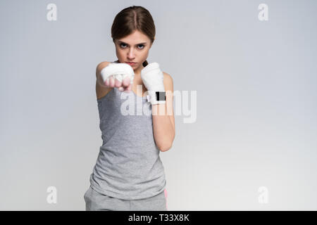 Beautiful boxer girl wearing sportive clothing and gloves practicing in the studio over gray background, athletic body, healthy lifestyle Stock Photo